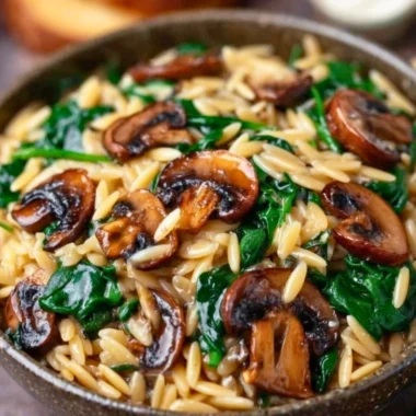 Garlic butter orzo dish with mushrooms and spinach garnished with herbs