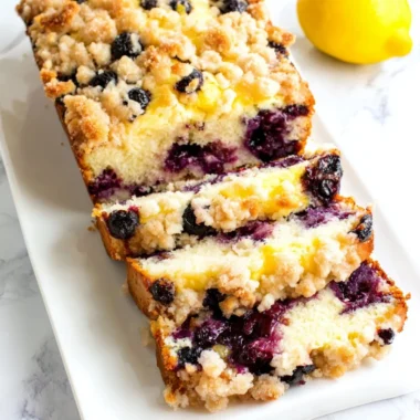 Sliced Blueberry Lemon Loaf on a wooden board with fresh blueberries and lemon slices.