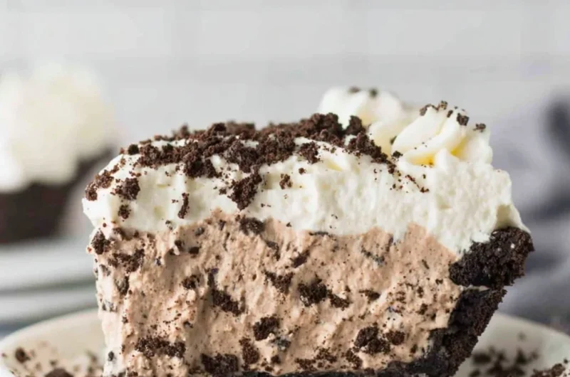 Delicious slice of Oreo Pudding Pie topped with whipped cream and chocolate shavings