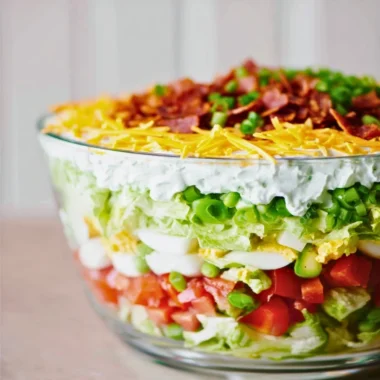 Seven layer salad with colorful ingredients in a clear serving dish