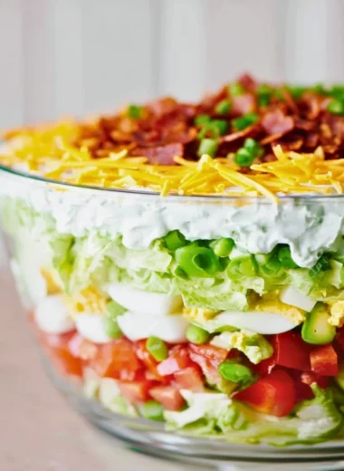 Seven layer salad with colorful ingredients in a clear serving dish
