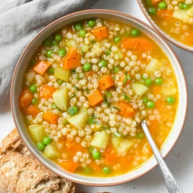 A steaming bowl of homemade barley soup with vegetables and herbs.