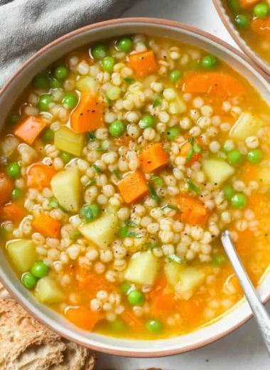 A steaming bowl of homemade barley soup with vegetables and herbs.
