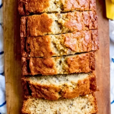 Slice of homemade banana bread with ripe bananas on a wooden table.