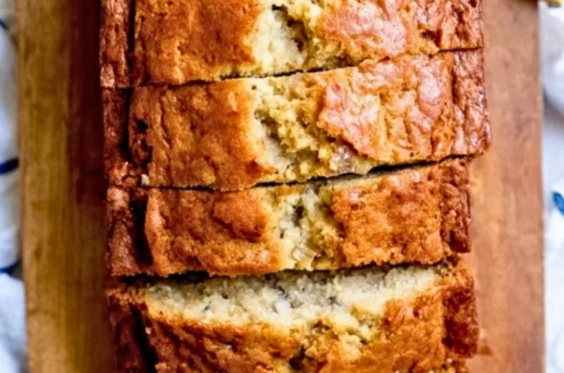 Slice of homemade banana bread with ripe bananas on a wooden table.
