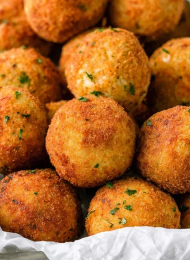 Crispy cheesy rice balls (arancini) served on a plate, garnished with herbs.
