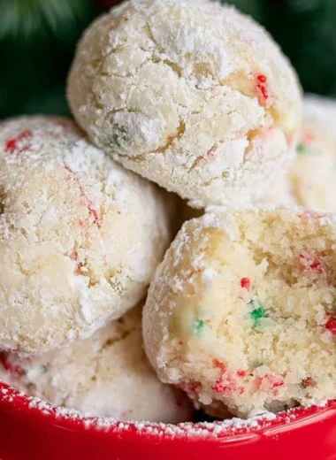 Baked snowball cookies dusted in powdered sugar on a festive plate.